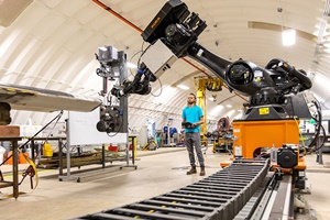 NREL researcher Hunter Huth stands beneath a robotic arm designed to automate a portion of the blade manufacturing process. Photo by Werner Slocum, NREL NREL researchers utilise robotics for wind turbine blade manufacturing 300 200